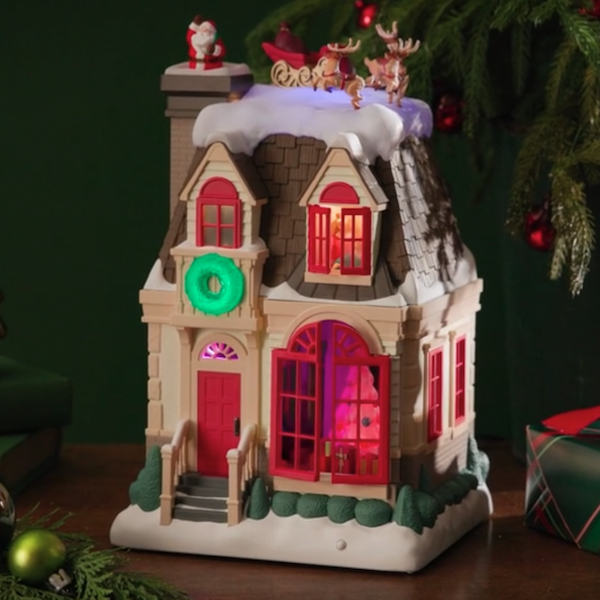 A Keepsake table decoration featuring a holiday house with different vignettes that can be seen through the lighted windowpanes.